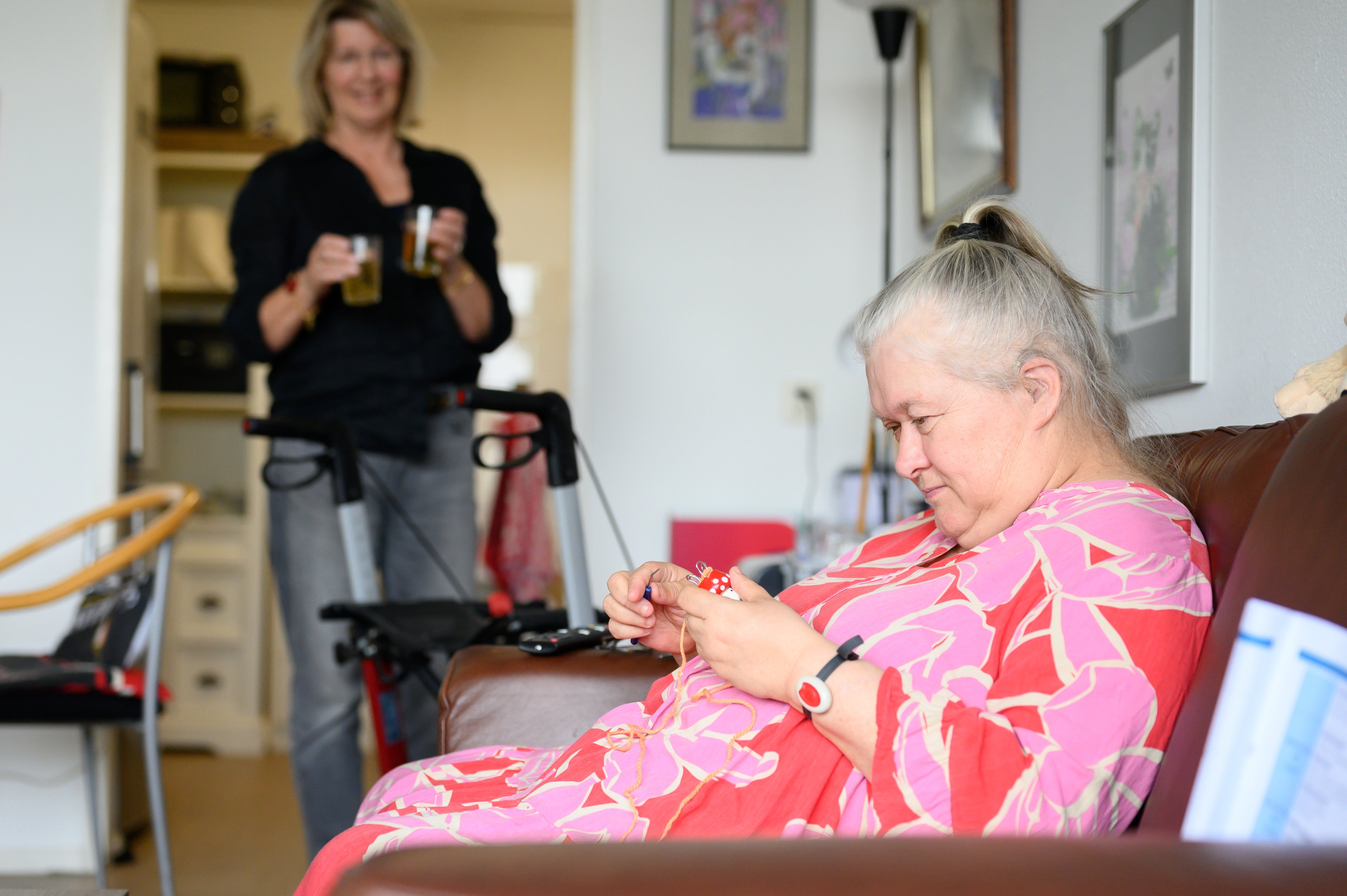 Een vrouw op de bank met handwerk, terwijl een begeleider drinken brengt